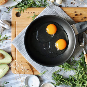 Profi Edelstahl-Bratpfanne 20cm with two cracked eggs in a frying pan on a wooden cutting board.