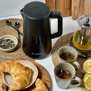 Wasserkocher 1.5 Liter von Klamer in eleganter Schwarzfarbe, umgeben von Tee, Tassen und einem Croissant.